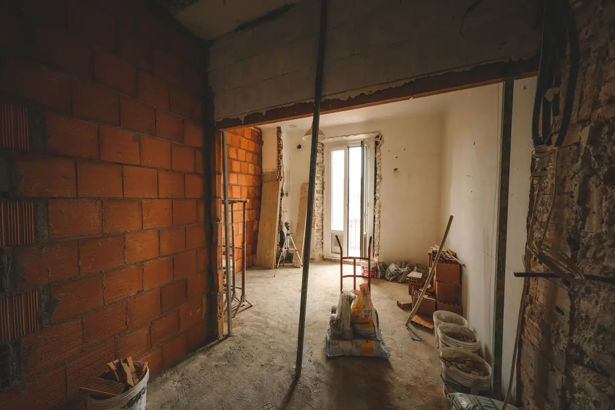 A wide opening knocked through a brick wall between two rooms, with a temporary prop still in place