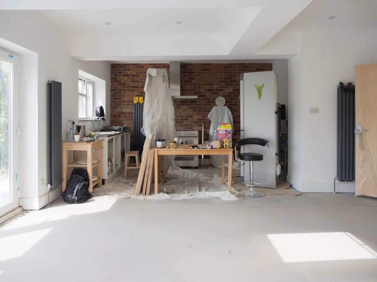 Inside a newly plastered rear extension: white walls, a bare floor, tall radiators and a brick chimney breast at the far end