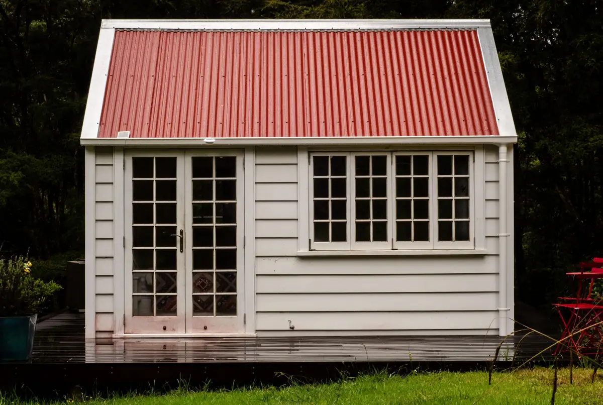 A white weatherboarded garden room with glazed French doors and a row of small-paned windows, set on a timber deck