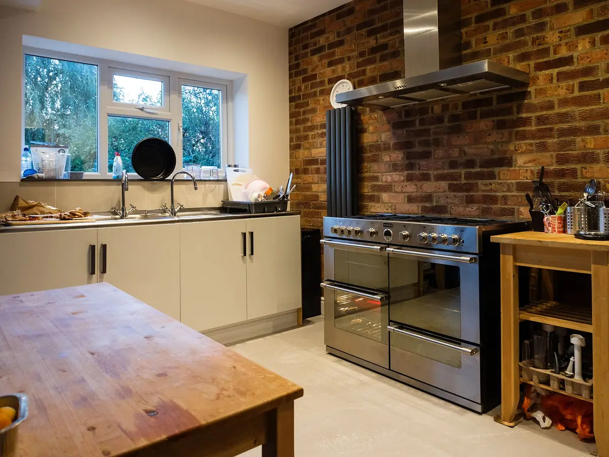 A finished kitchen in an extension, with an exposed brick wall, a range cooker under a steel hood and a wooden worktable