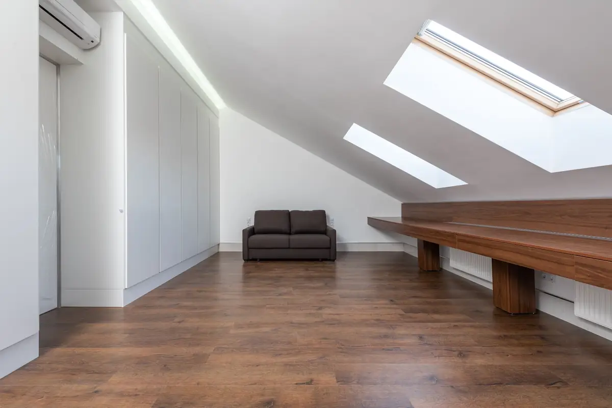 A loft room with two roof windows in the slope, built-in white wardrobes, a long wooden desk and a small sofa