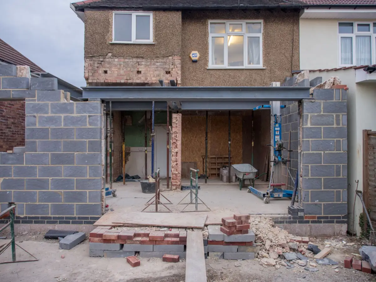 The back wall of a semi-detached house opened up, with a steel beam on props and new blockwork walls rising either side