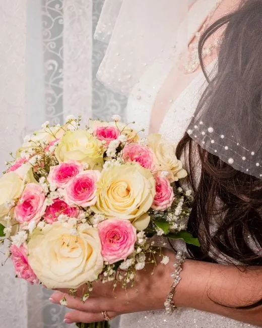 A soft wedding bouquet of pink and cream roses tied with ribbon