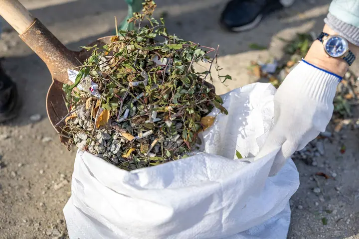 A spade tipping weeds and garden waste into a white builder's bag