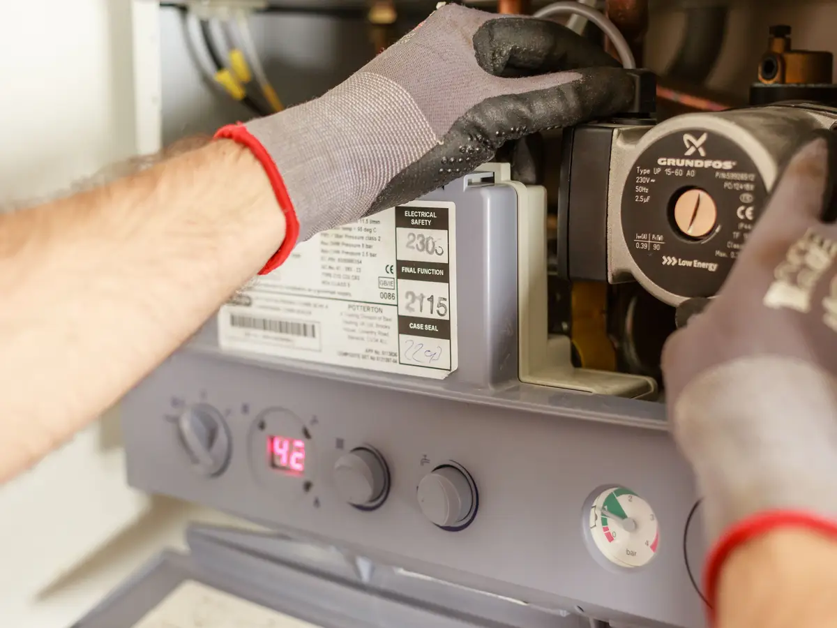 Gloved hands working on the pump inside an open gas boiler, its pressure gauge and display below