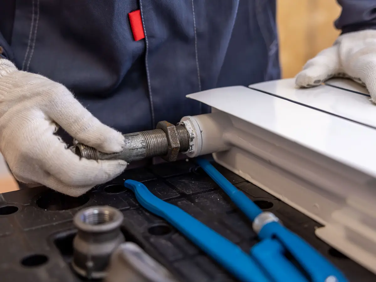 A plumber in work gloves tightening a fitting on the end of a new radiator