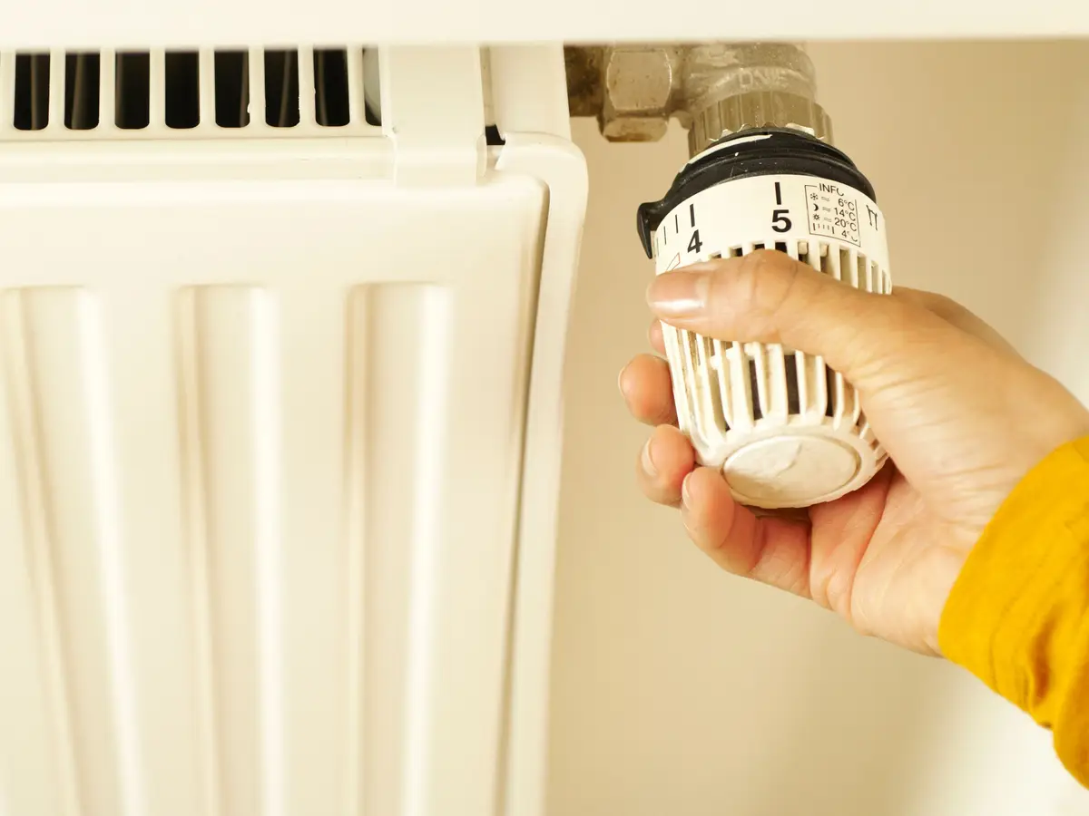 A hand turning the thermostatic valve on a white panel radiator