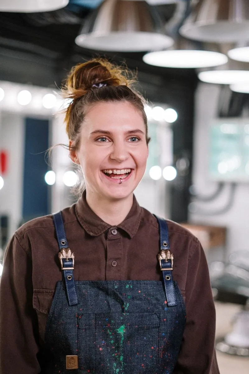Mia Rowe, senior stylist, laughing warmly in her work apron on the salon floor