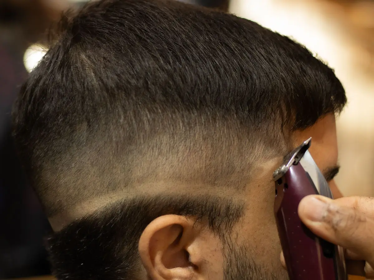 A barber's clippers blending a skin fade above a client's ear
