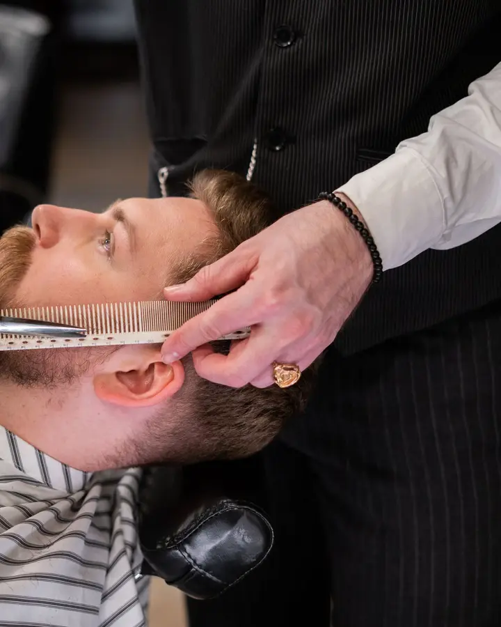 A barber setting a client's beard line with scissors and a comb
