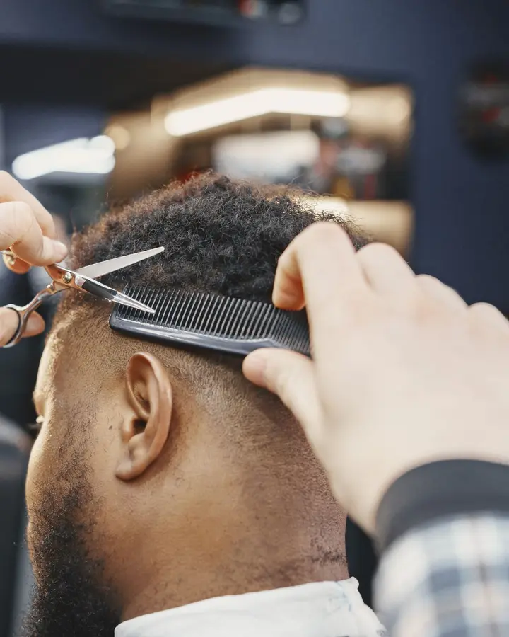 A barber cutting short curly hair with scissors over a comb