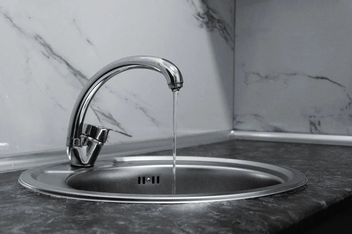 Gleaming chrome kitchen tap with water running into the sink