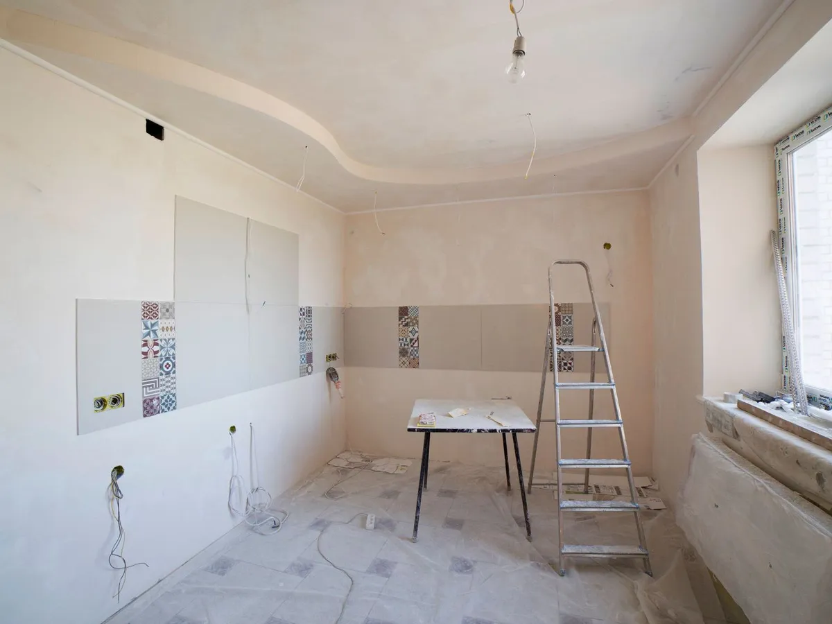 A room mid-renovation: bare plaster walls, dust sheets on the floor, a stepladder and a trestle table