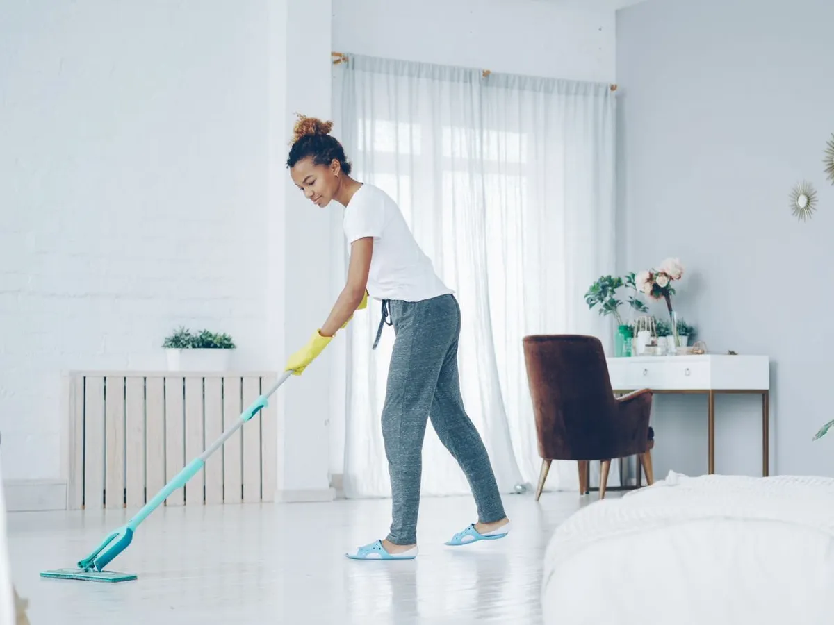 A cleaner in yellow gloves mopping the floor of a bright white living room